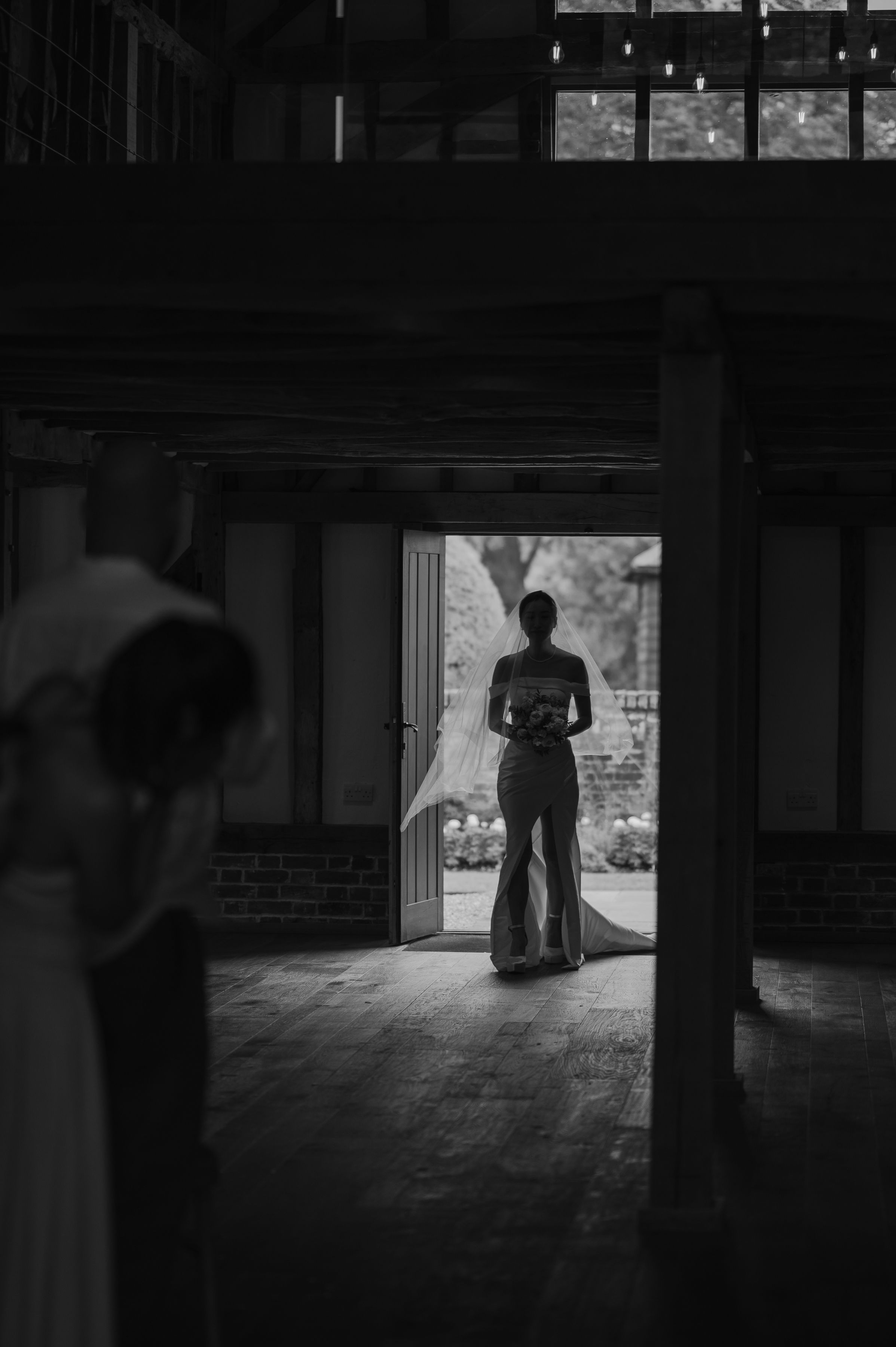 A silhouetted figure stands in a doorway, creating a moody black and white composition with dramatic lighting.