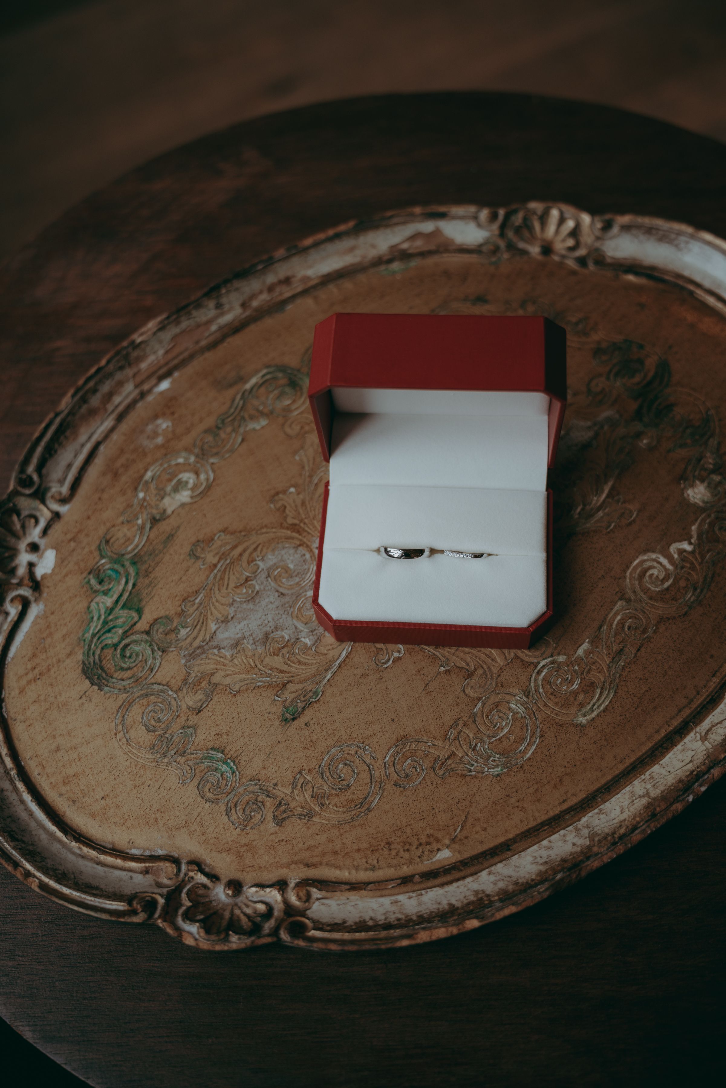 Diamond engagement ring in red box sits on ornate antique silver serving tray with decorative patterns.