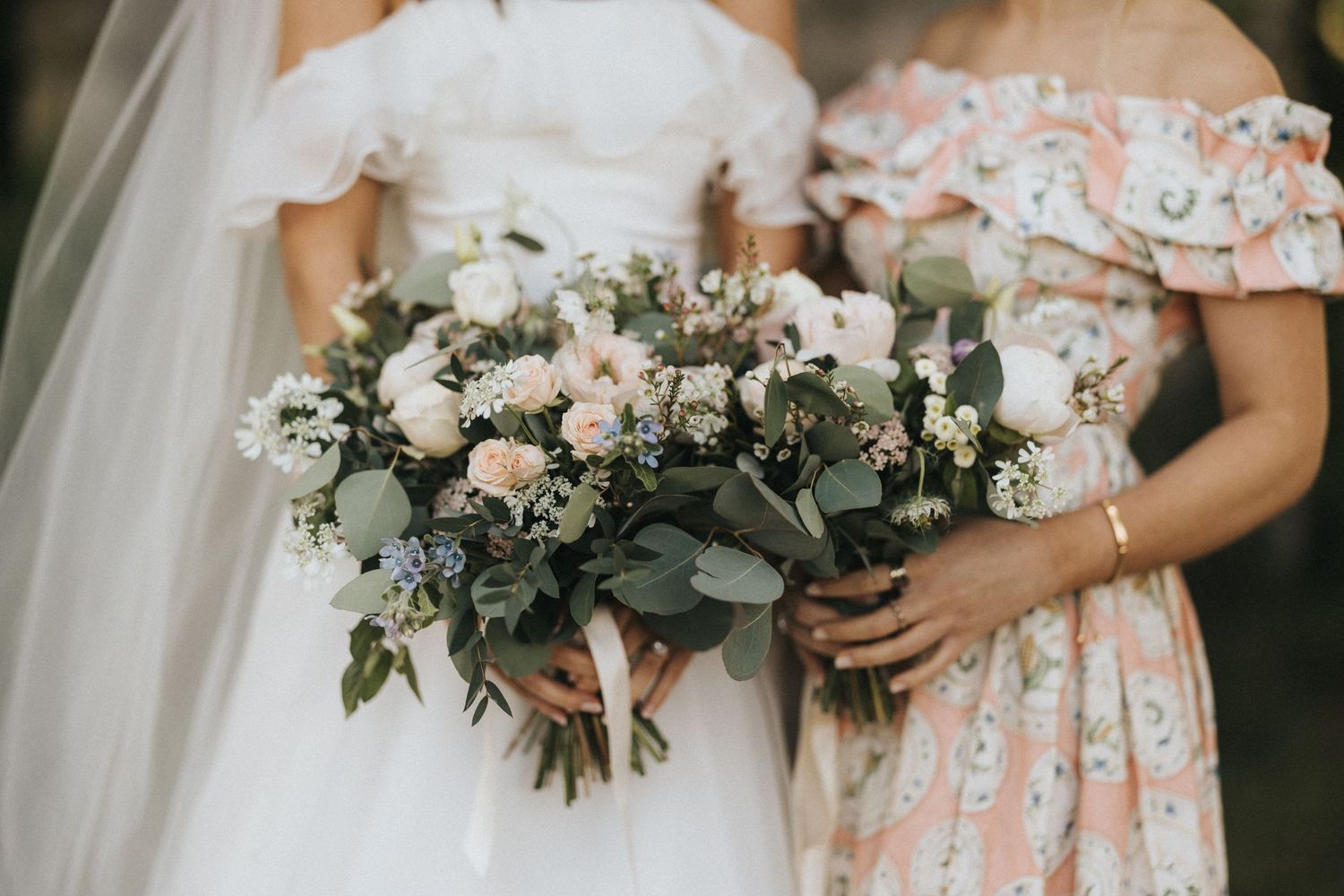 Beautiful wedding bouquets with blush roses, eucalyptus and greenery held against white dress and floral print dress.