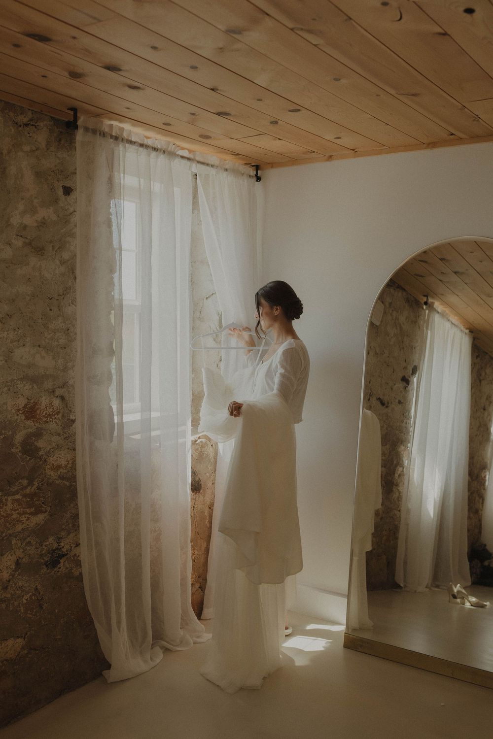 Ethereal bridal portraits in a rustic room with white curtains and natural light.
