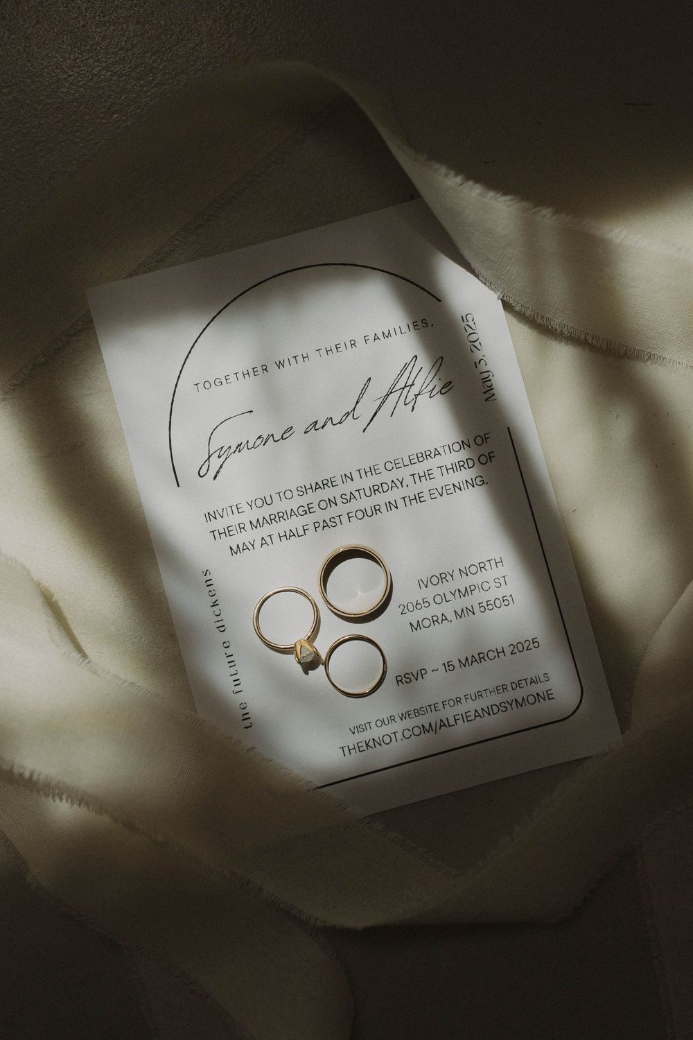 Elegant wedding invitation with gold text and rings in dramatic lighting.