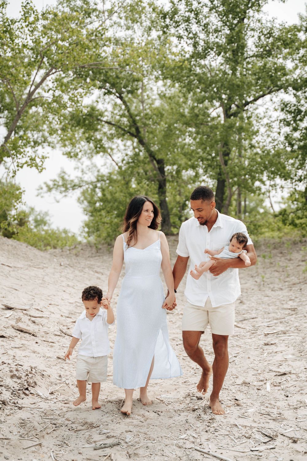 Family enjoys a sunny beach day walk together wearing coordinated white outfits on the sandy shore.