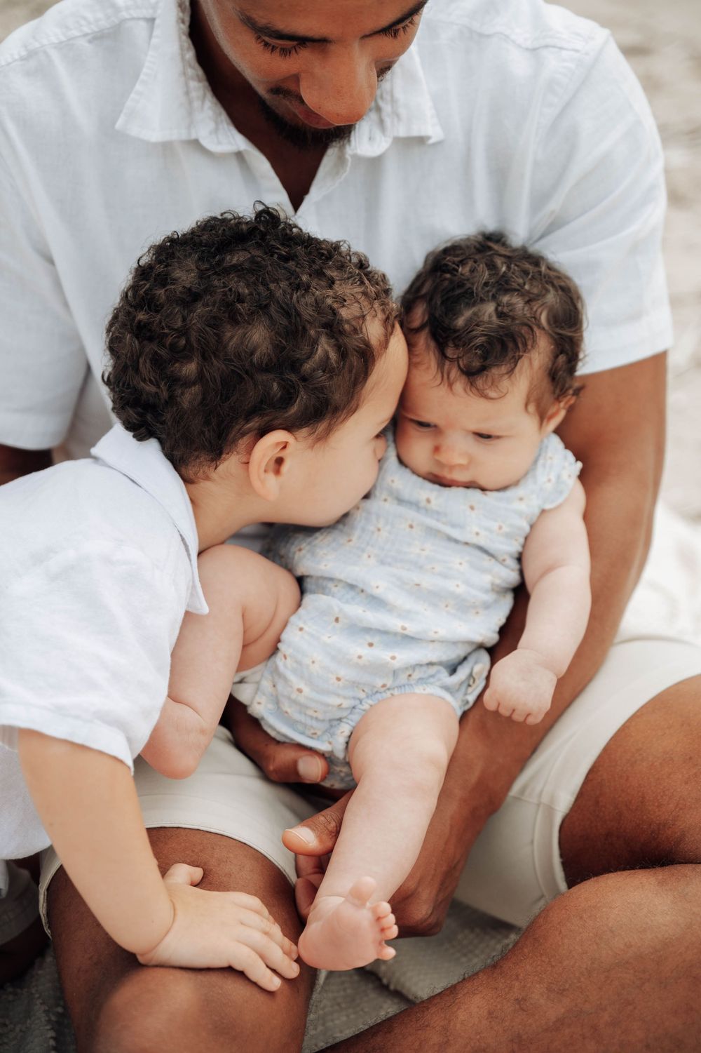 A tender moment as a parent in a white shirt embraces and interacts with a small child wearing white and grey.