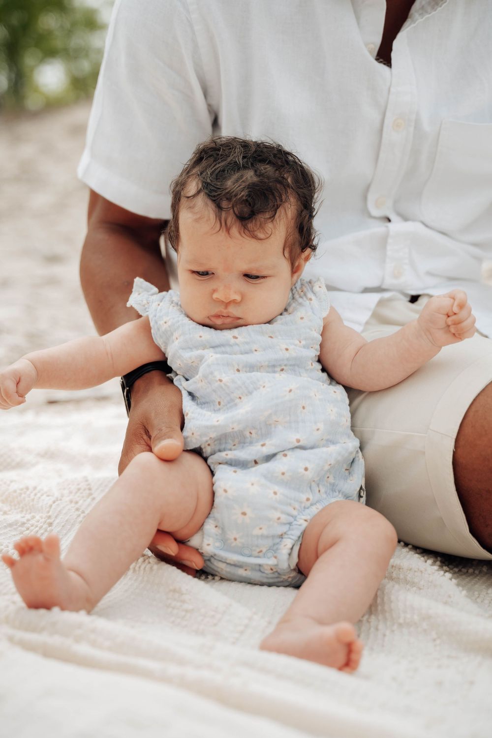 Close-up series of a baby lying on a white blanket wearing a light blue and white polka dot romper.