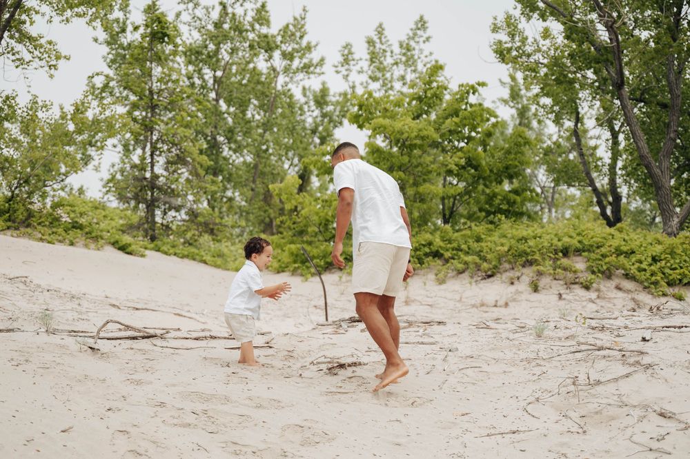 A person in a white dress walking along a sandy beach path through coastal vegetation on a sunny day.