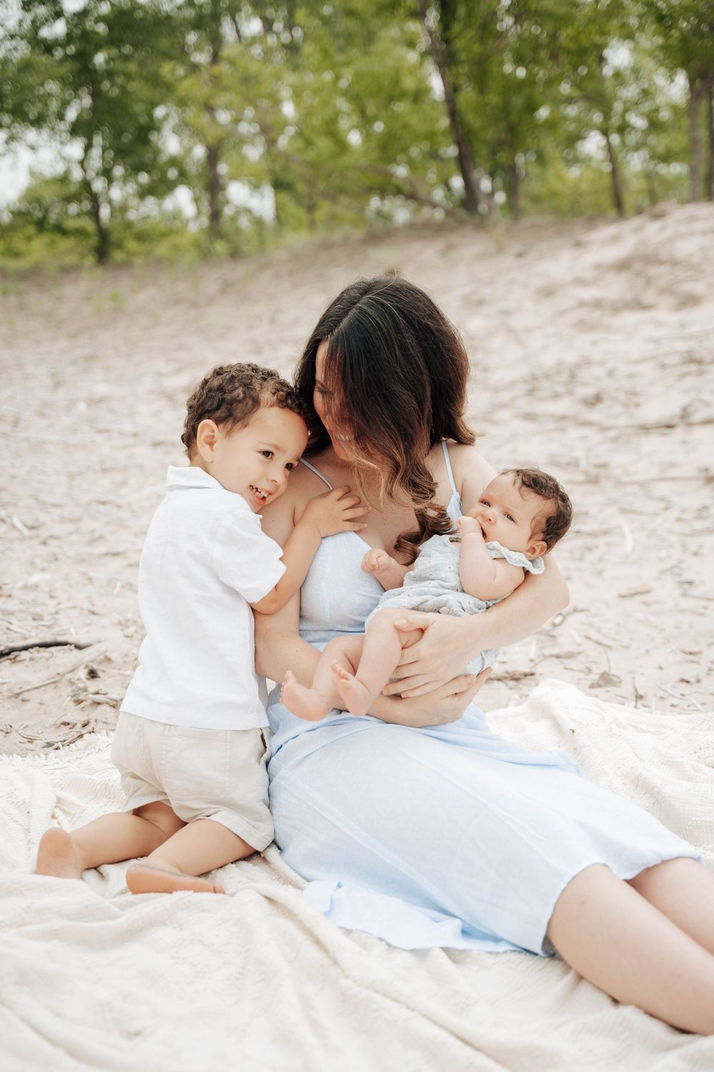 A tender family moment shared together on a sandy beach at sunset with everyone wearing white and light blue outfits.