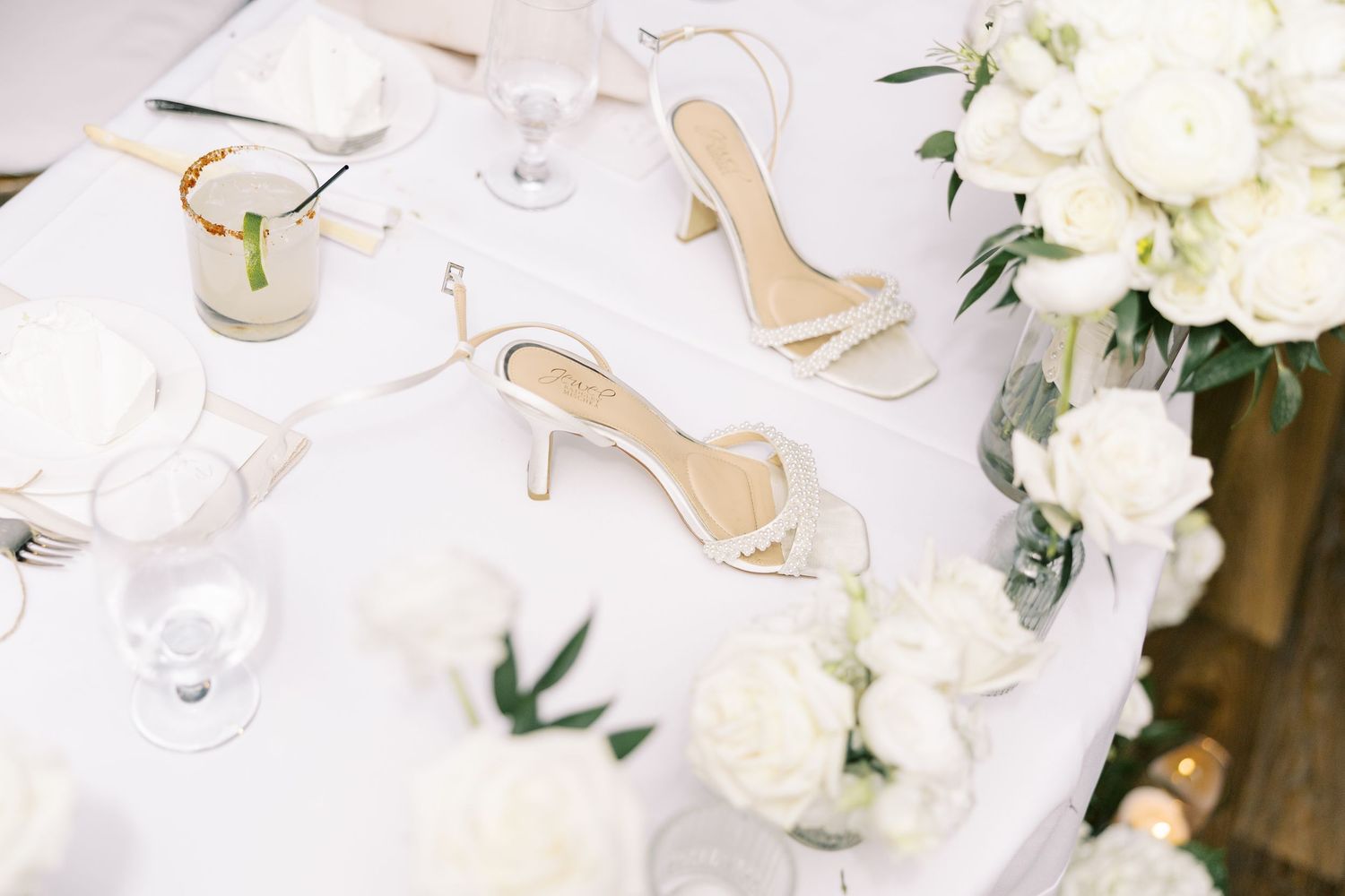 Elegant place setting with gold flatware and wine glasses surrounded by white floral arrangements and greenery.
