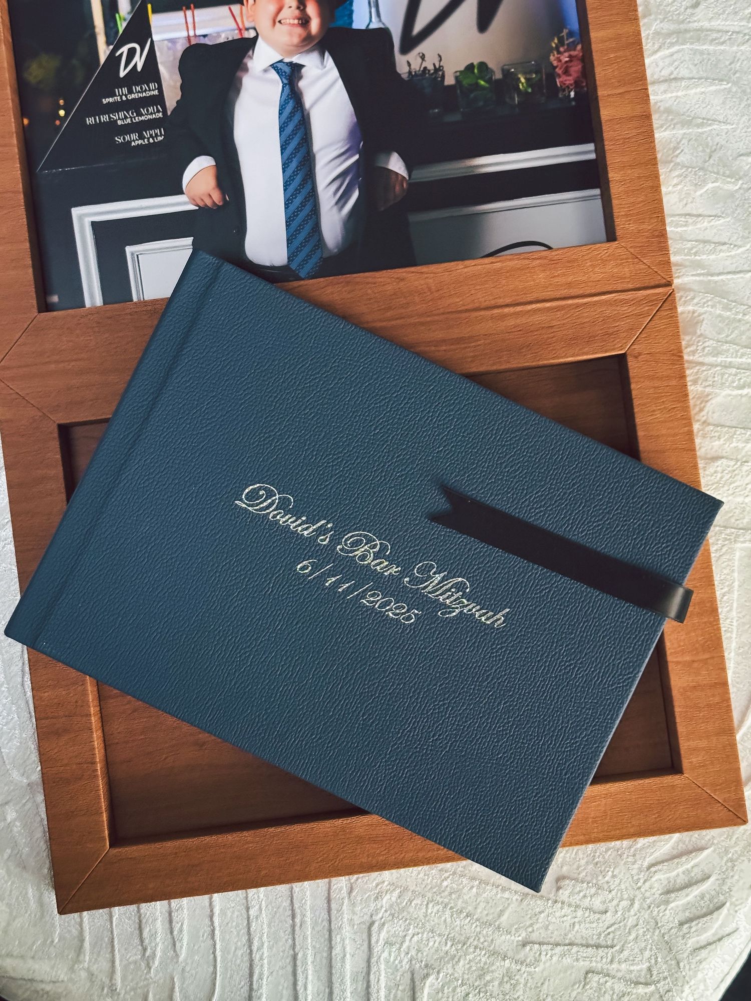 Elegant navy blue wedding album books with names embossed on covers arranged on wooden surface.