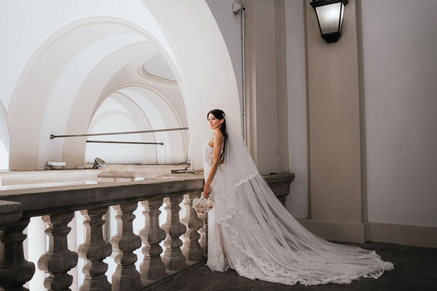 A long white wedding dress train elegantly trails down a curved hallway with classic architectural details.