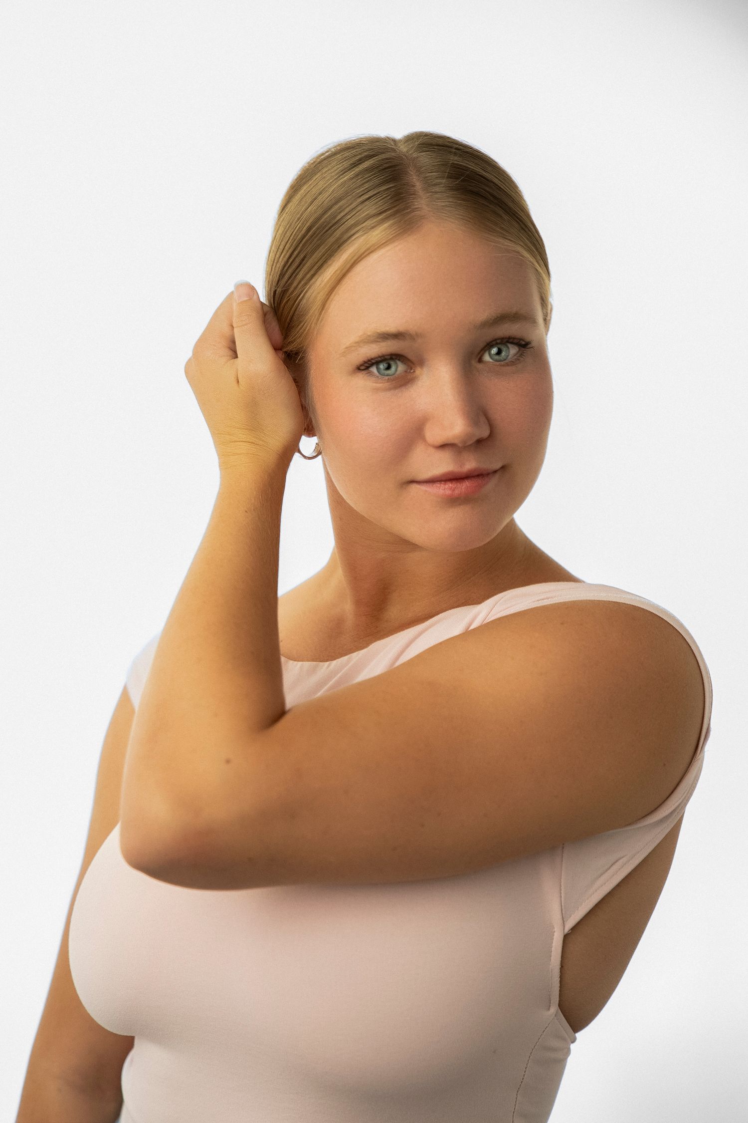Portrait of a person in a white sleeveless top posing with hand raised against a light background.