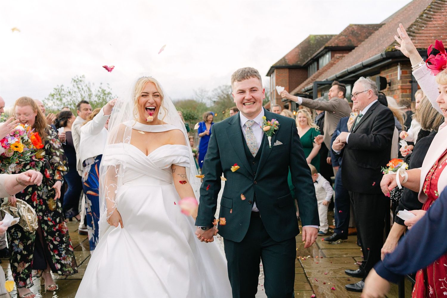 Wedding guests shower newlyweds with colorful confetti as they walk down the outdoor aisle together after the ceremony.