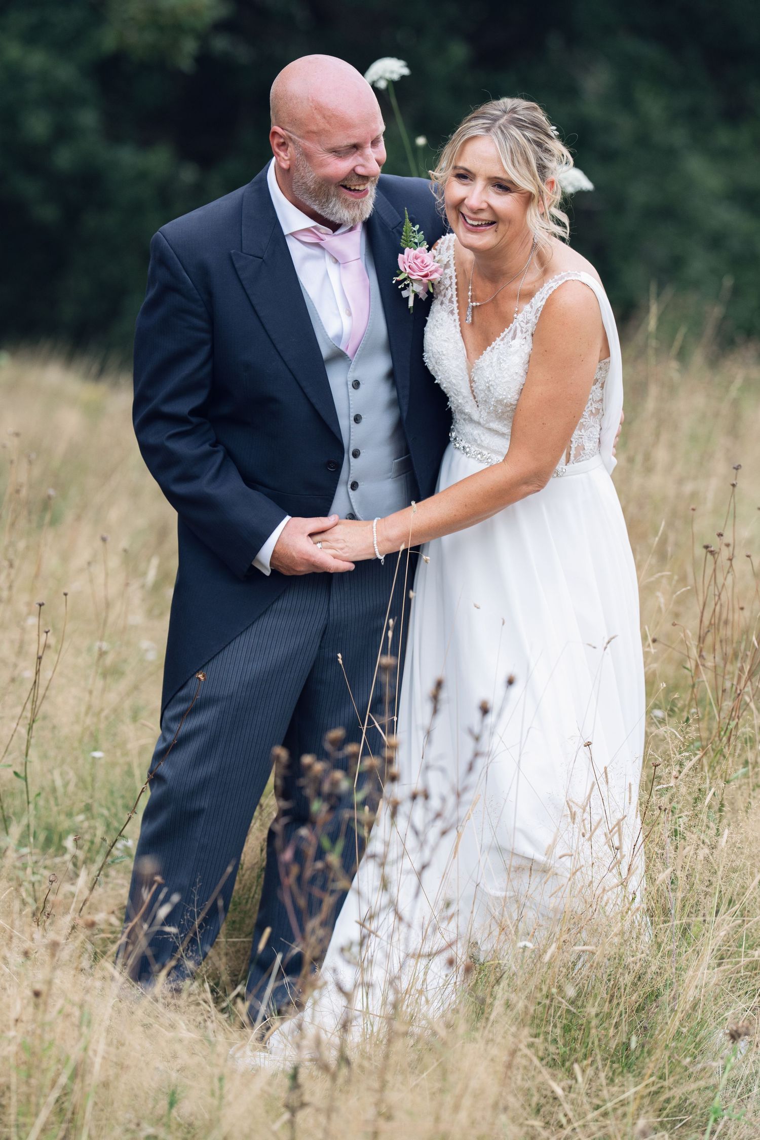A wedding portrait of a couple standing in a meadow of tall grass, bride in white dress and groom in formal suit.