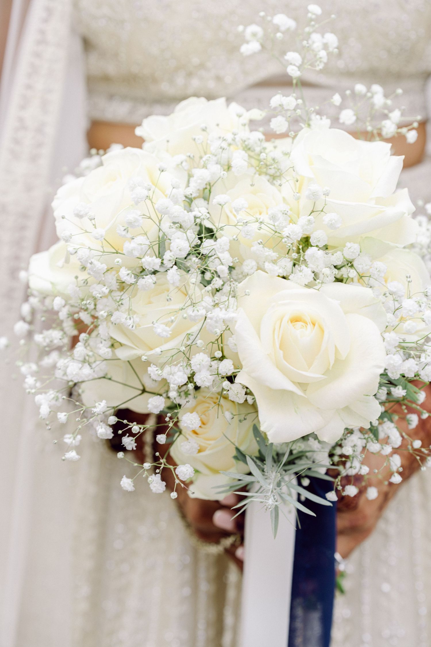 White roses and baby's breath bouquets with navy blue ribbon wraps arranged in a row for a wedding ceremony.