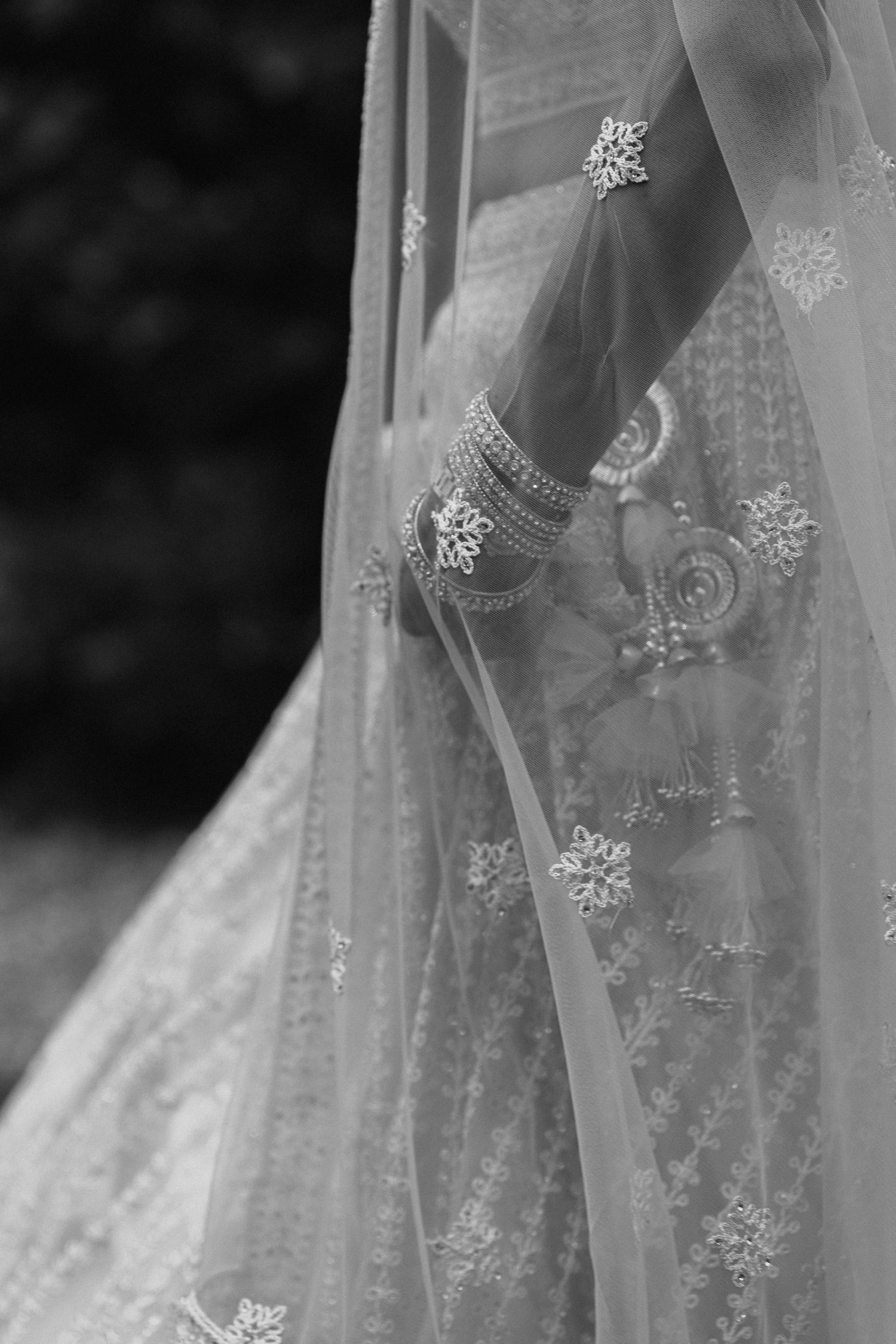 Close-up black and white photo of an ornate wedding dress with delicate lace details and intricate beaded embellishments.