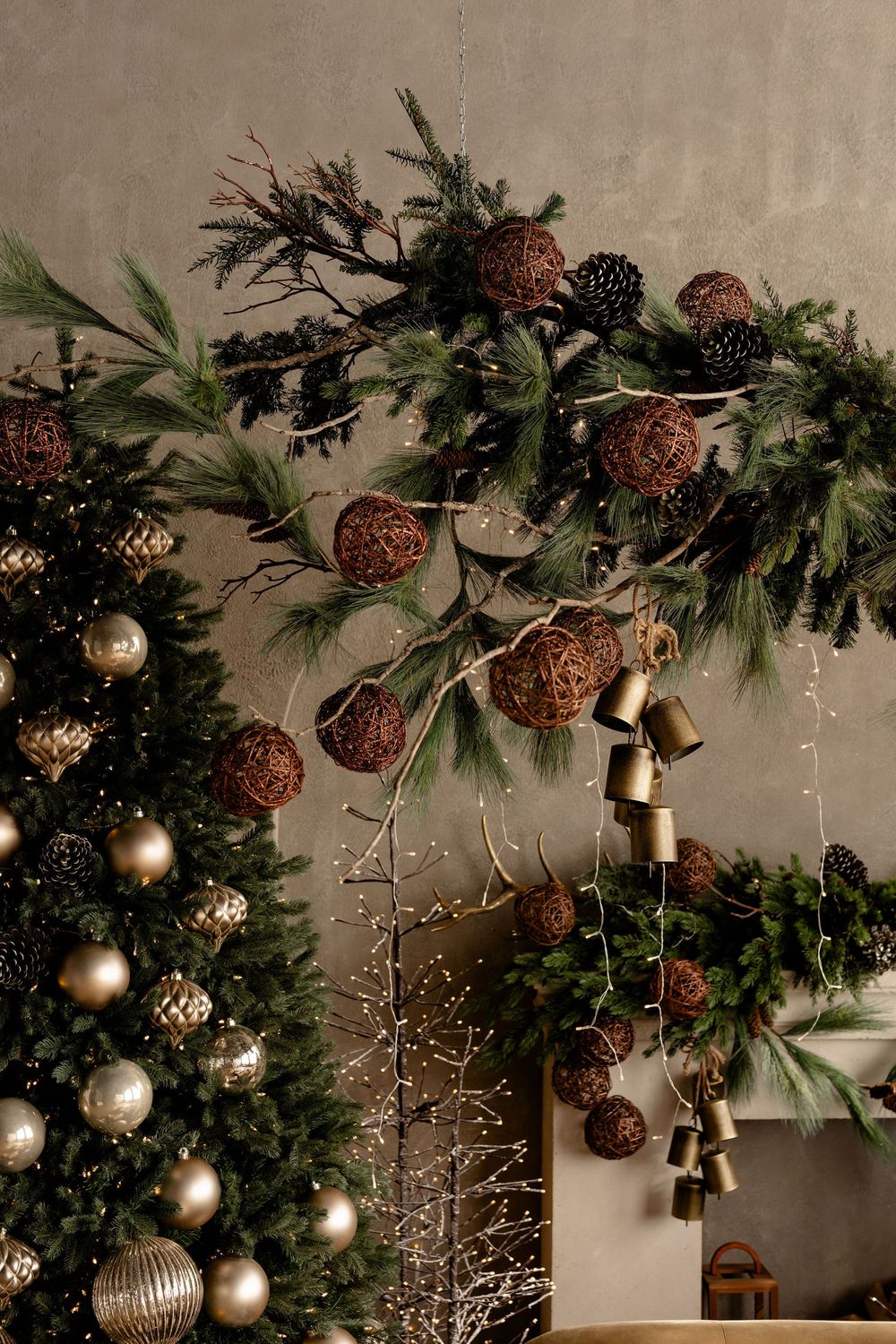 Rustic Christmas decor featuring pinecones, metallic baubles, and evergreen garland against a neutral wall.