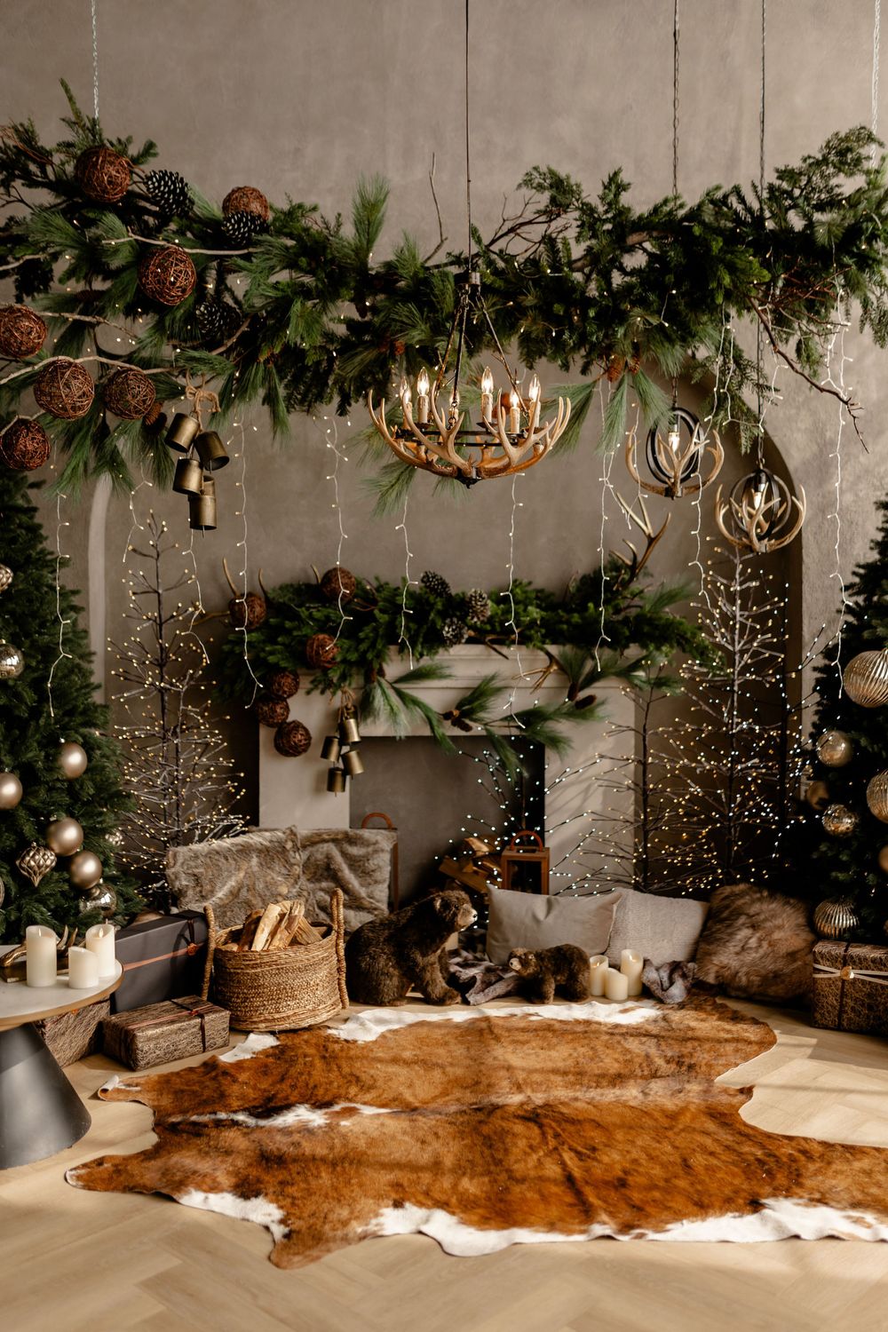 Cozy Christmas scene with antler chandeliers, fur rug, and evergreen garland decorating a rustic fireplace setting.