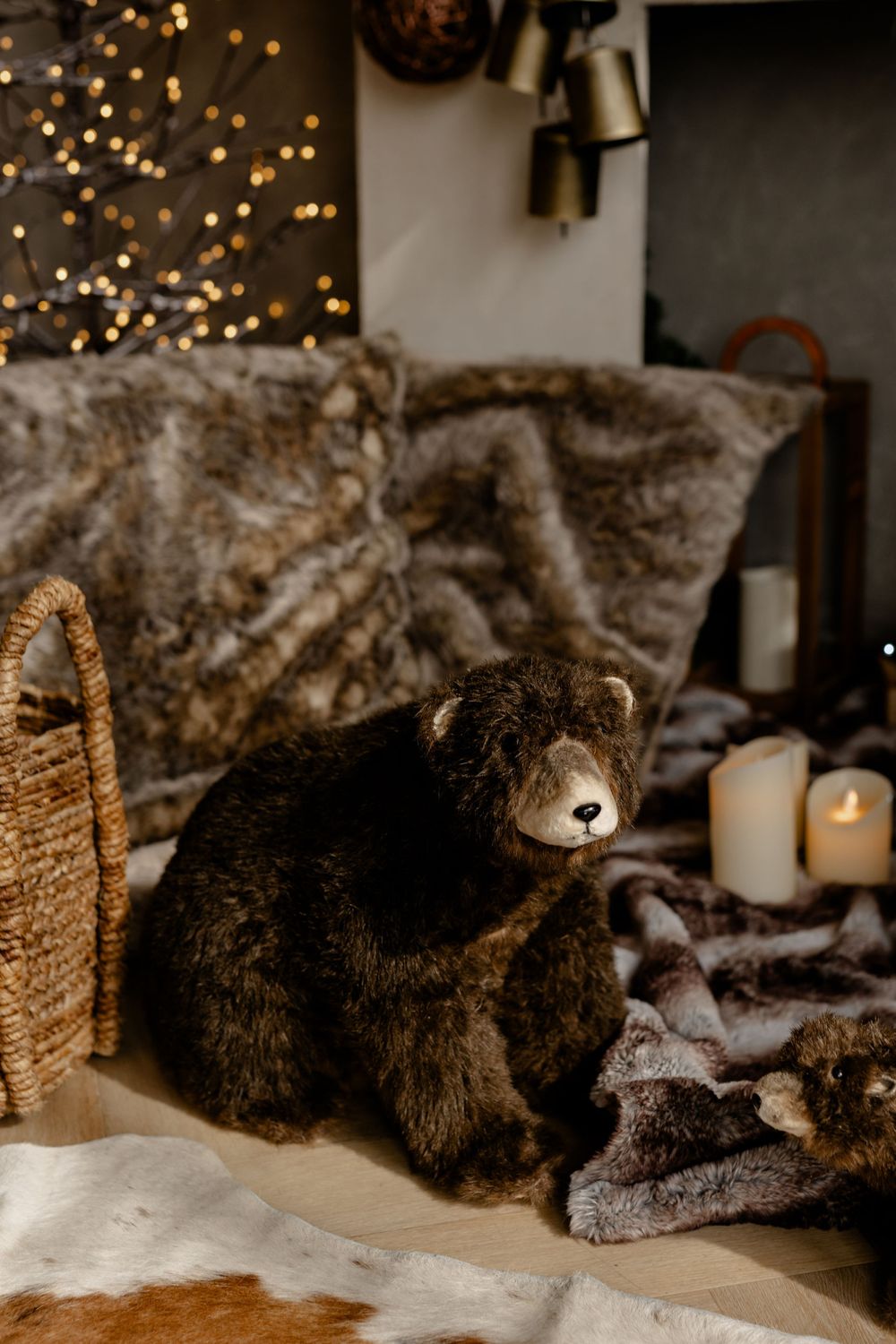 Black kitten curled up sleeping on cozy gray fur blanket with candlelight and twinkle lights in background.