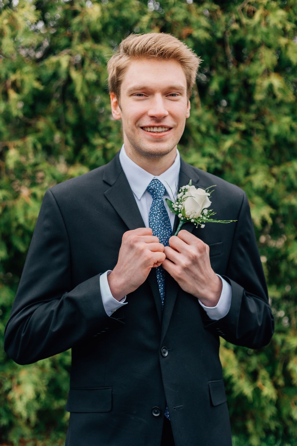 Groom adjusting boutonniere while wearing navy suit with floral tie.