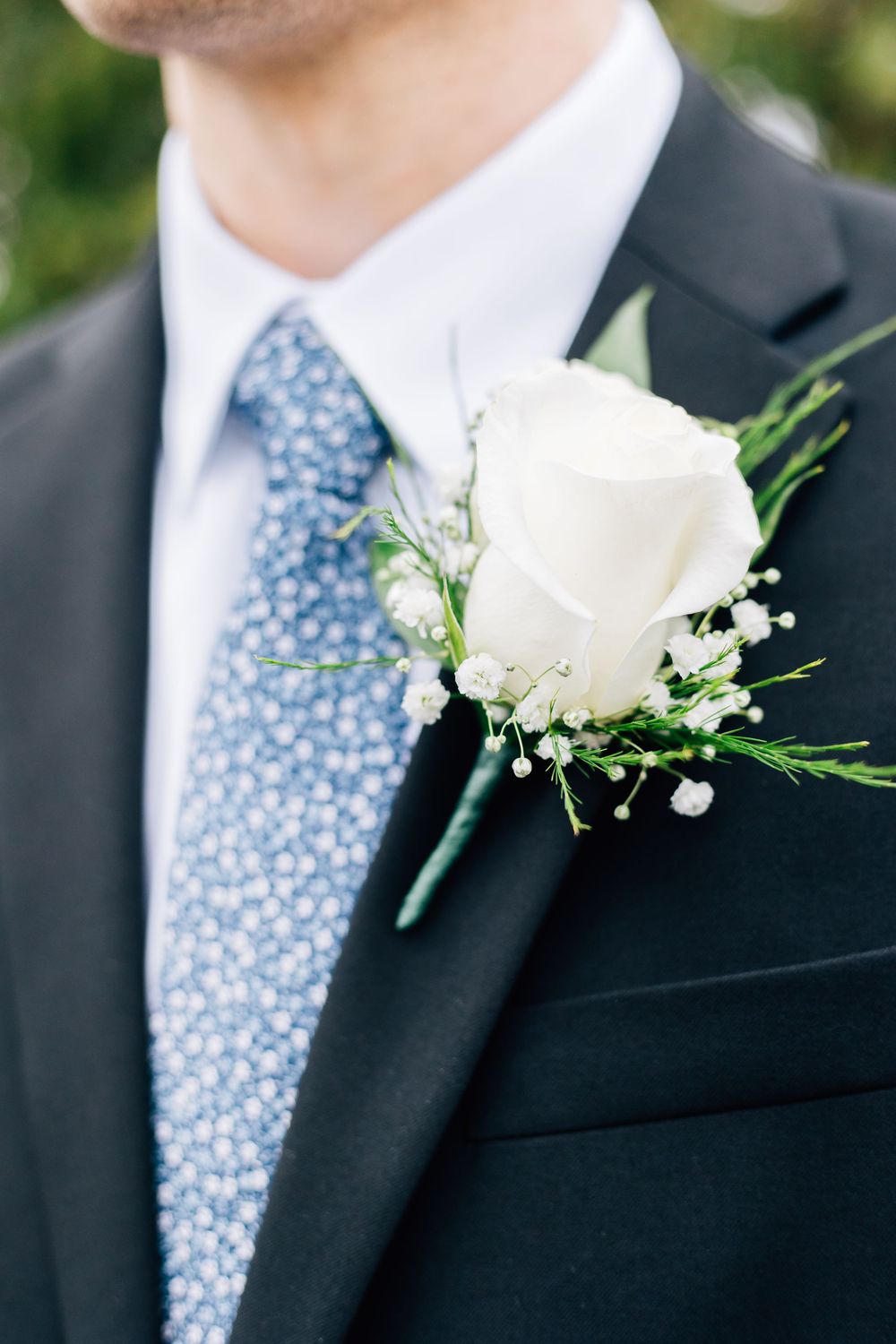 Detailed shot of white rose boutonniere with baby's breath on navy suit lapel.