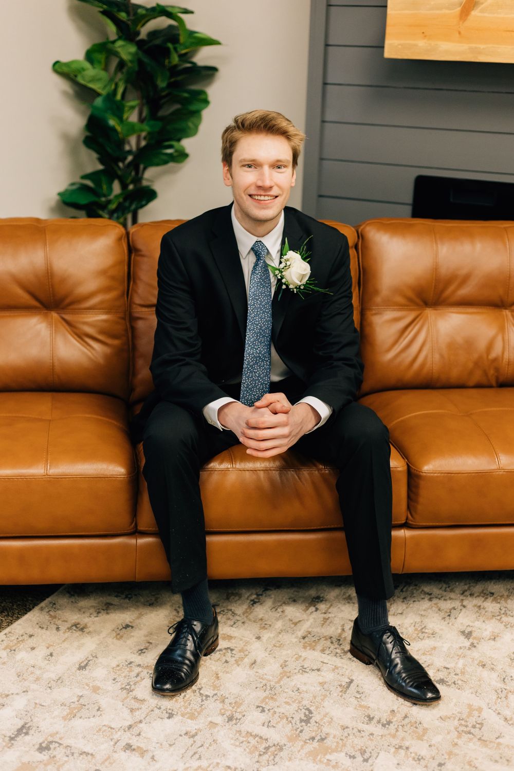 Wedding day portrait on brown leather couch with indoor plant decor.