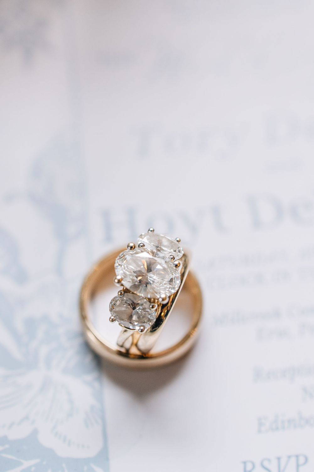 Close-up of diamond engagement ring and wedding band on light blue background.
