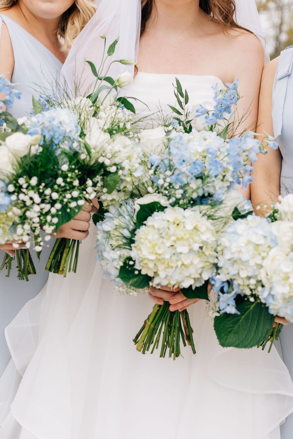 Detailed shot of bridal party bouquets with white hydrangeas and delicate blue flowers.