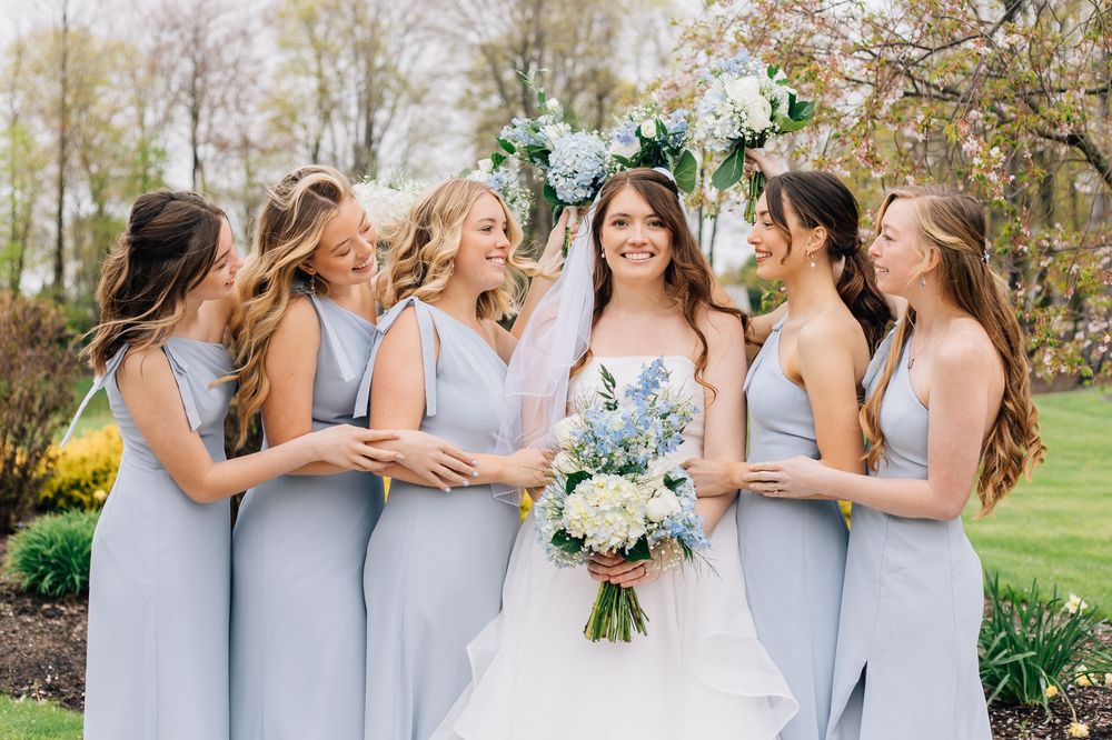 A bridal party in light blue dresses sharing a joyful moment outdoors.
