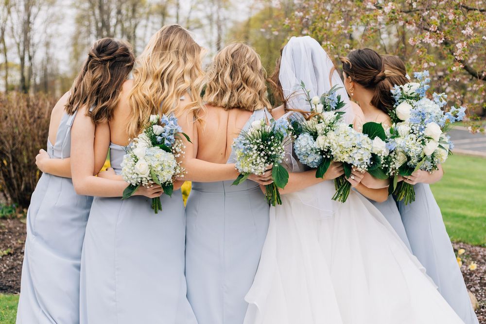 Back view of bridesmaids in blue dresses standing with bride outdoors.
