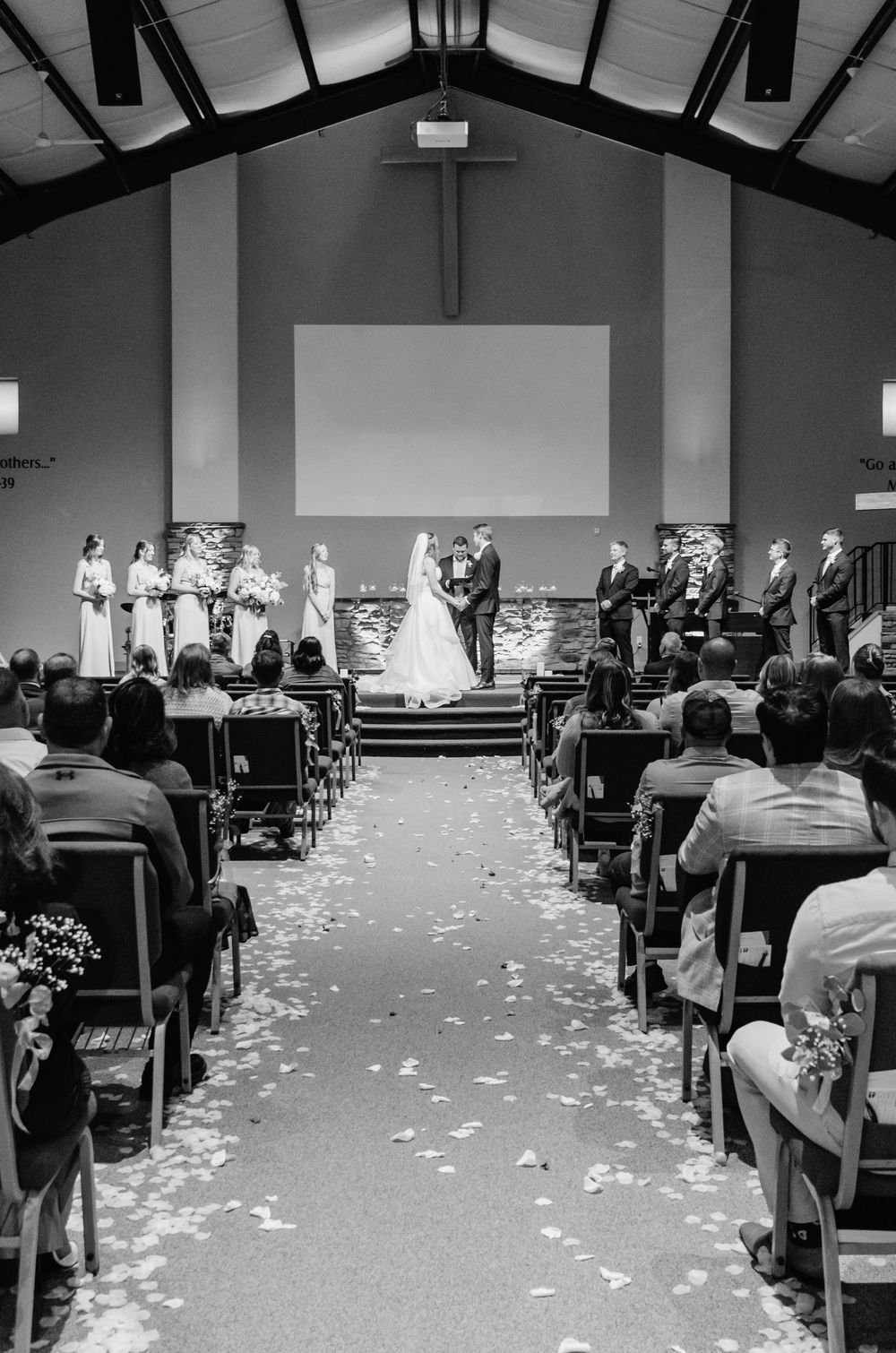 Black and white photo of wedding ceremony in church with rose petals lining the aisle.