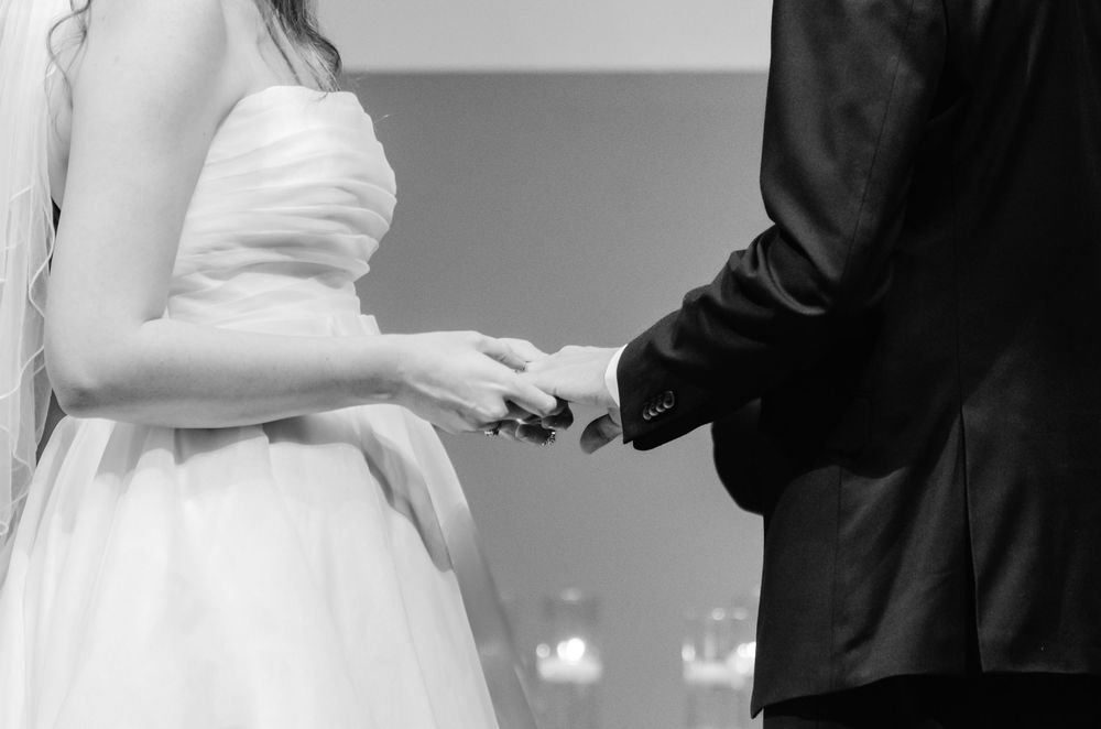 Black and white close-up of couple exchanging rings during wedding ceremony.