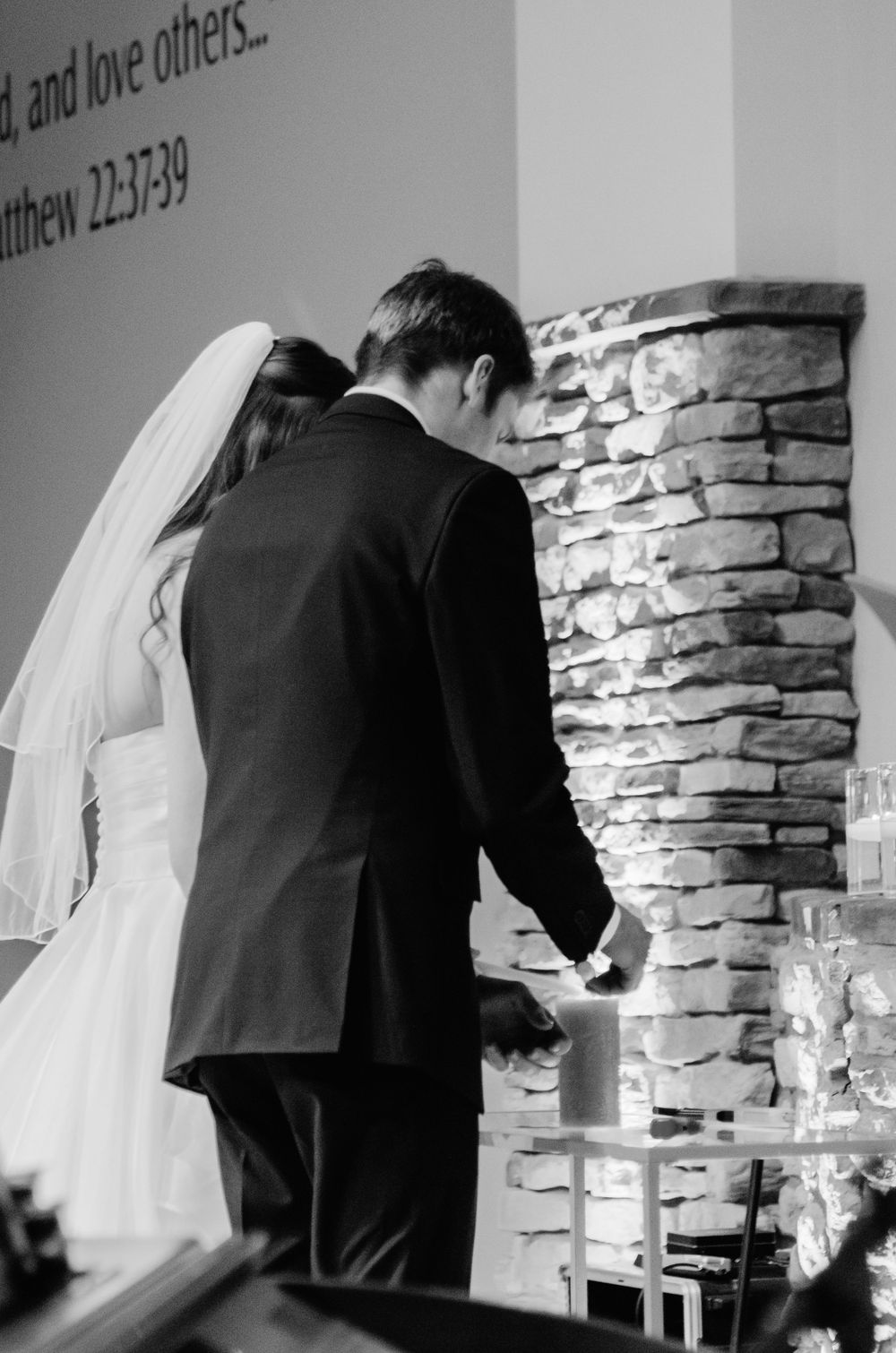 Black and white photo of couple lighting unity candle during wedding ceremony.