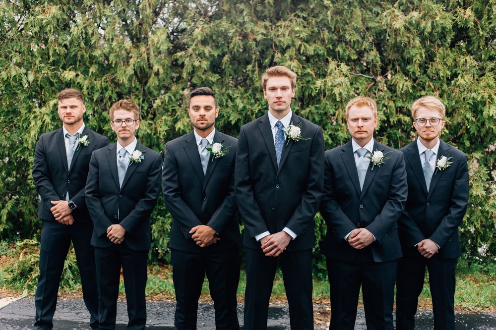 Groomsmen in black suits standing in a formal line outdoors.