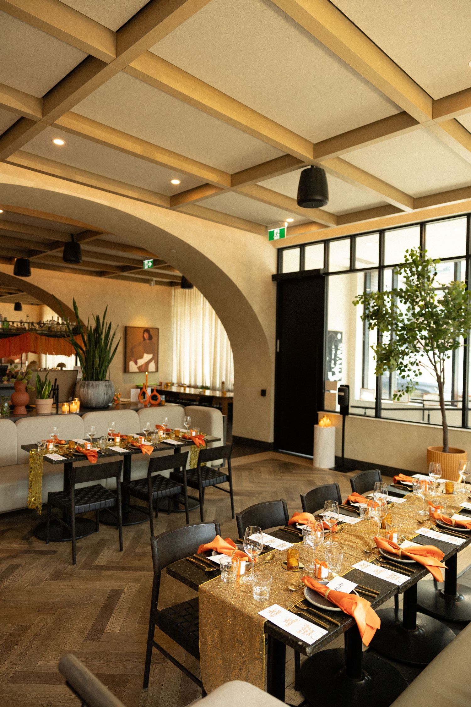 Modern restaurant interior with wooden tables set for dining and coffered ceiling details.