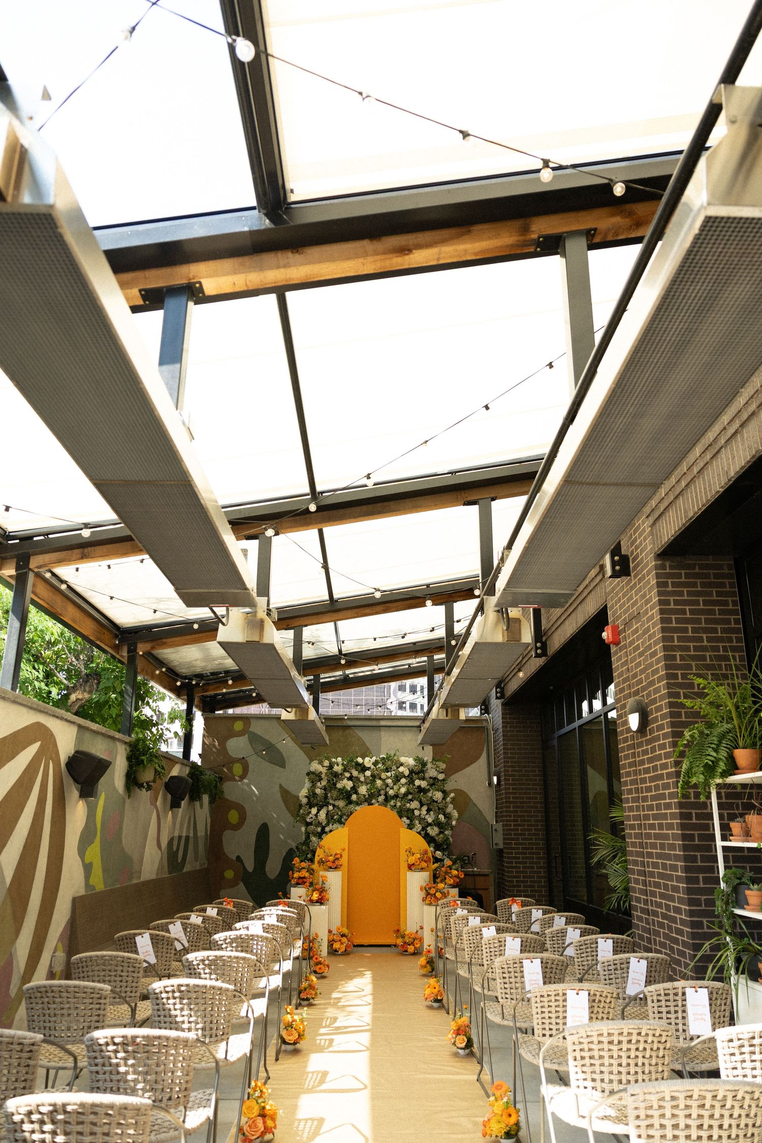 Modern event space with rows of white chairs under a glass ceiling and exposed brick walls with natural lighting.