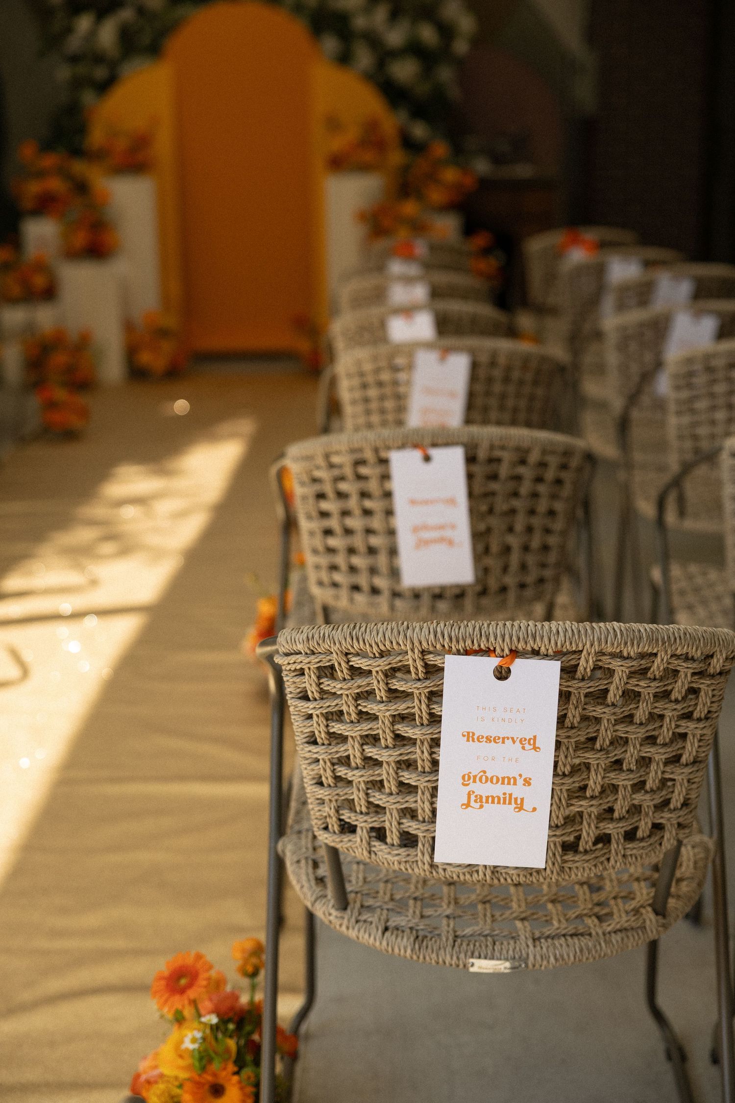 Woven reception chairs with name cards arranged in rows under natural lighting.