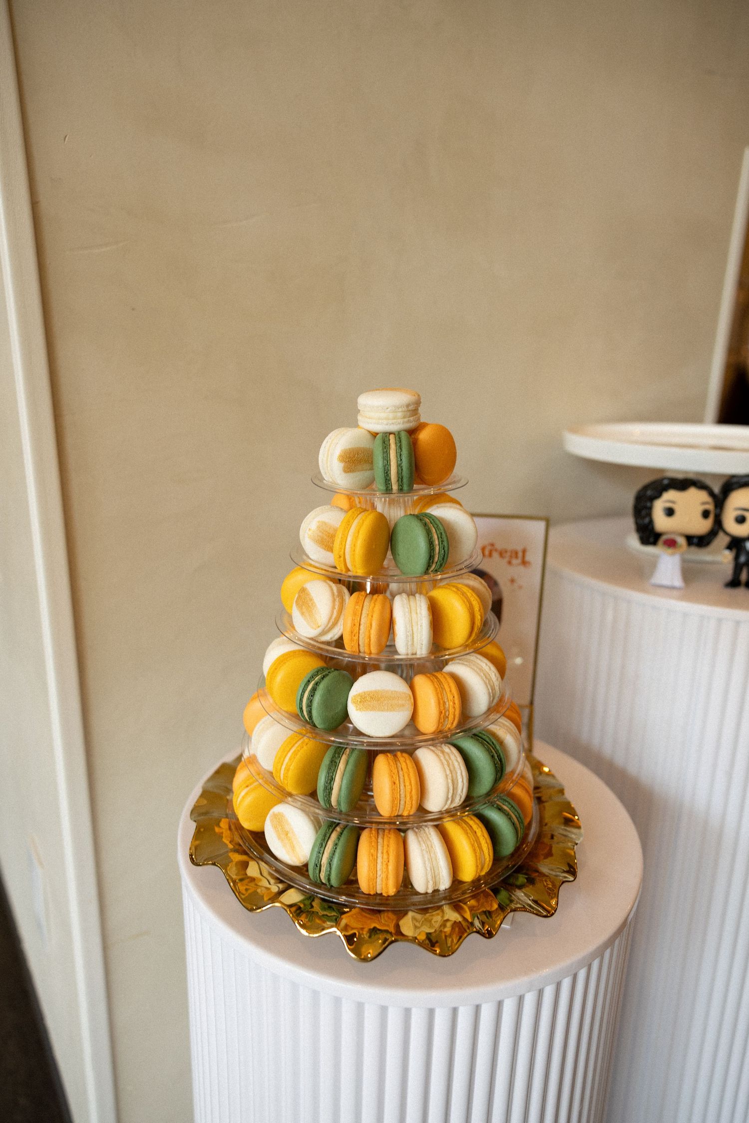 Elegant tiered macaron tower display in yellow and green hues on white pedestal.
