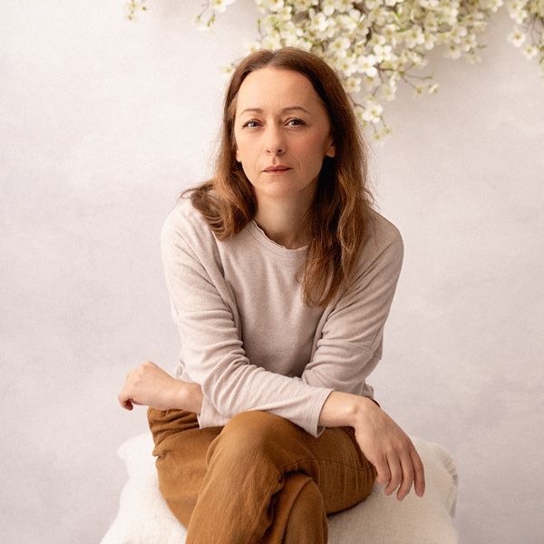 Professional portrait in soft lighting featuring casual attire with a white sweater and jeans against a neutral background.