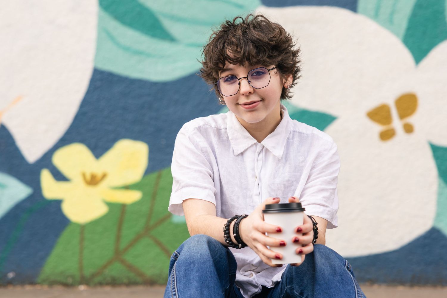 Four artistic photos show a person with glasses sitting casually against blue and white floral background patterns.