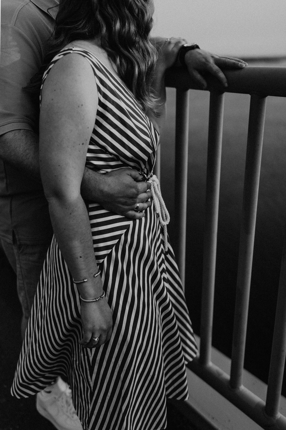 Black and white photo of a person wearing a striped wrap dress leaning against an outdoor railing.