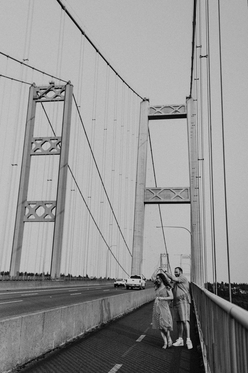 Two people and a dog stand on the Tacoma Narrows Bridge walkway, photographed in black and white.