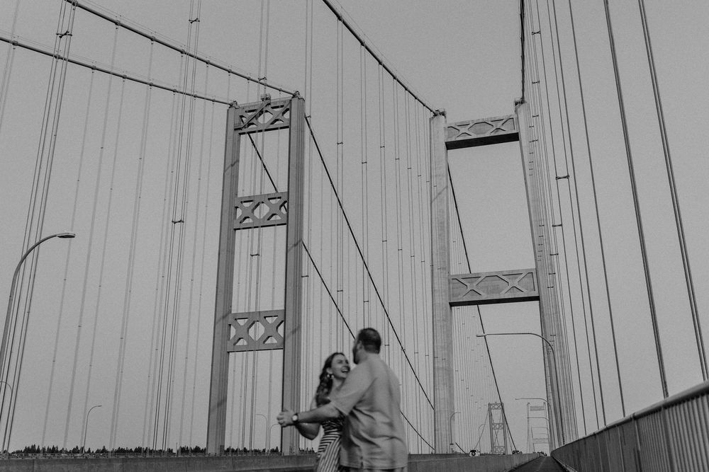 A romantic black and white moment between a couple on a suspension bridge with towering cables and beams.