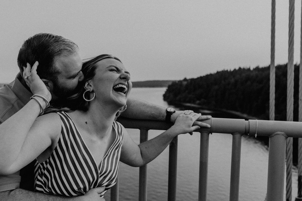 A joyful couple shares a tender moment together while standing on a boat deck overlooking a lake.