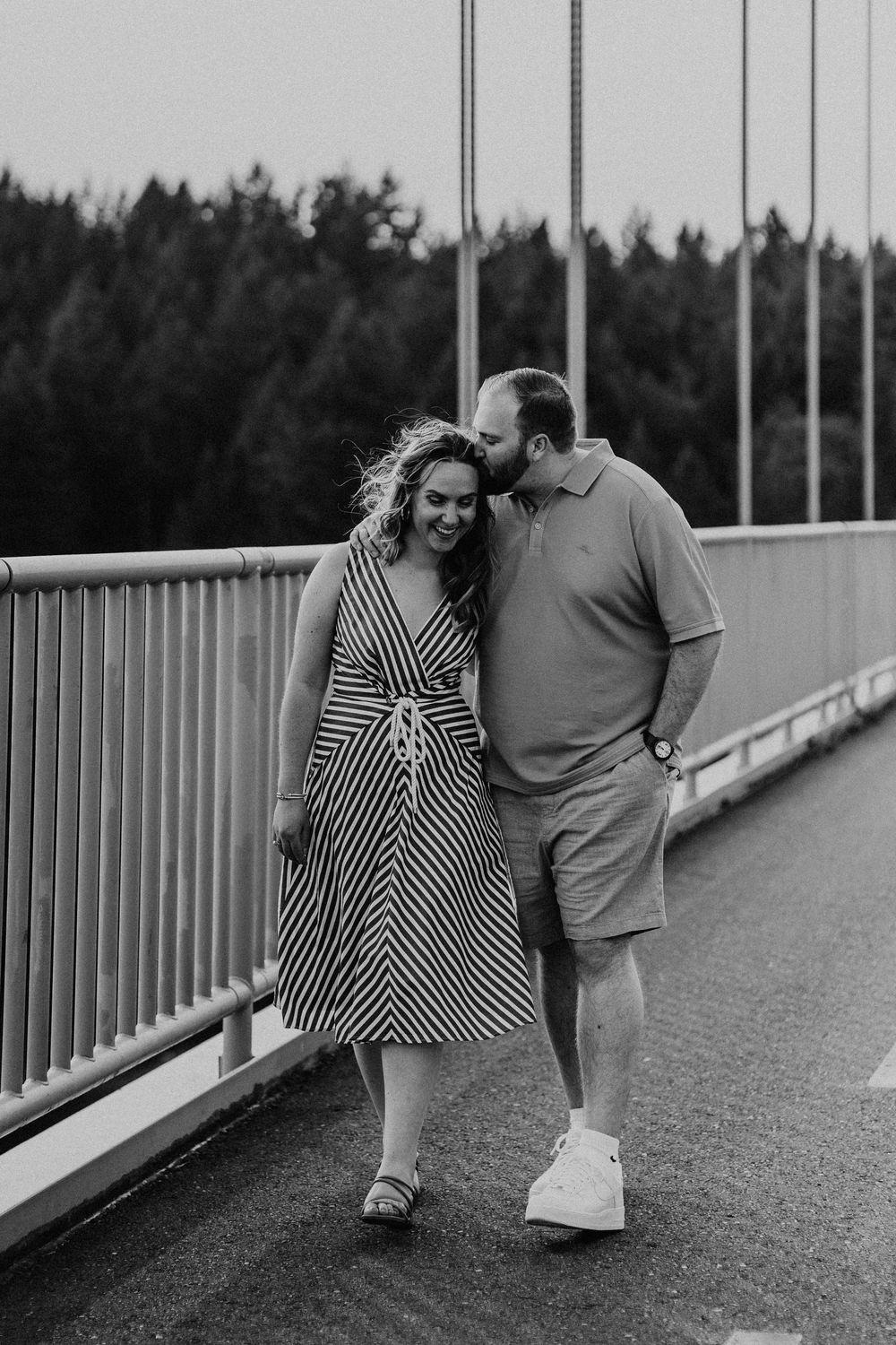 A couple in black and white share playful moments together on a bridge walkway creating a series of candid photos.