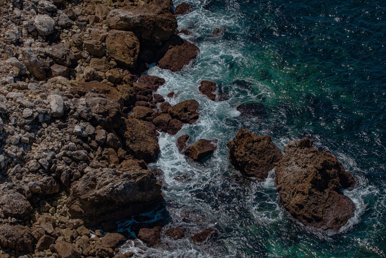 Dark rocky coastline with waves crashing against jagged cliffs creating dramatic ocean spray.