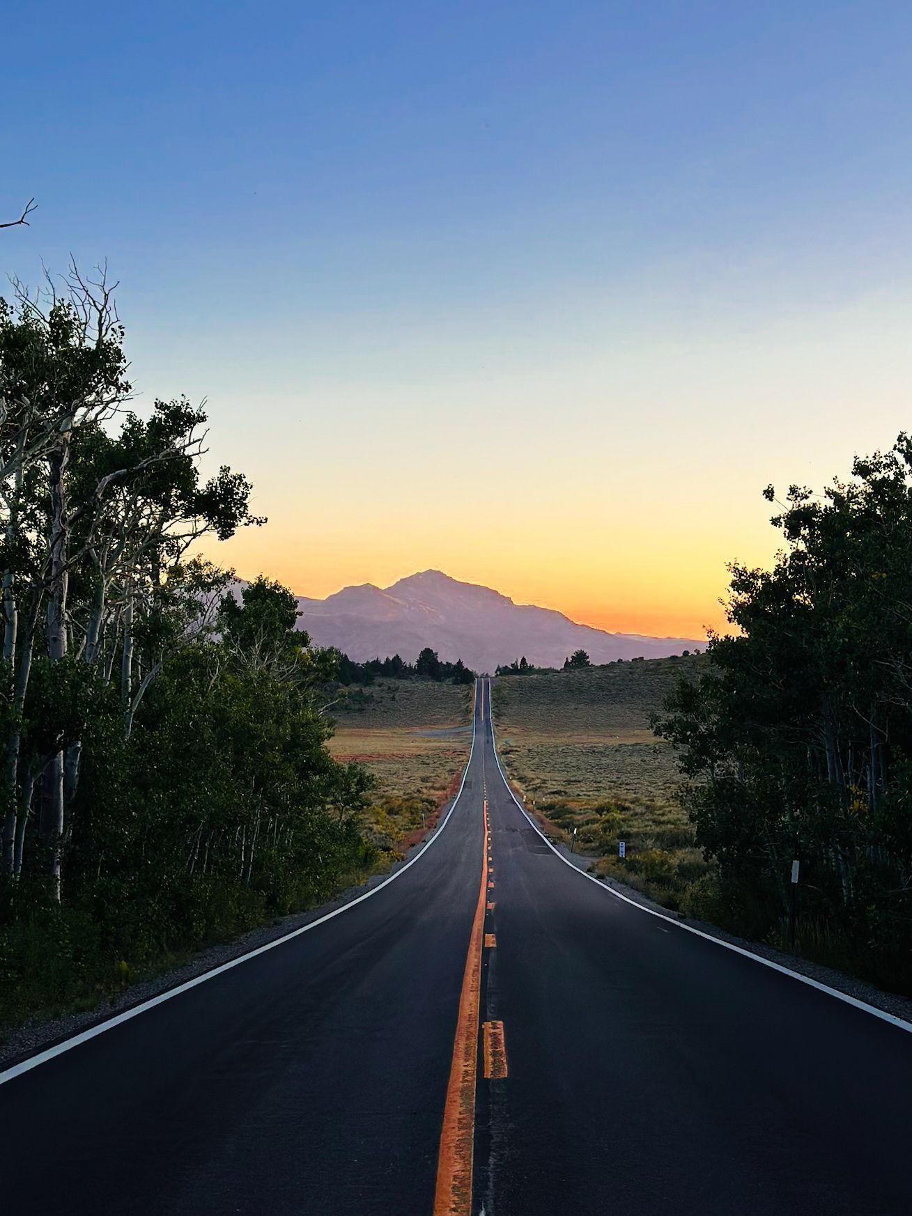 Long straight road leading to a mountain silhouette during sunset.