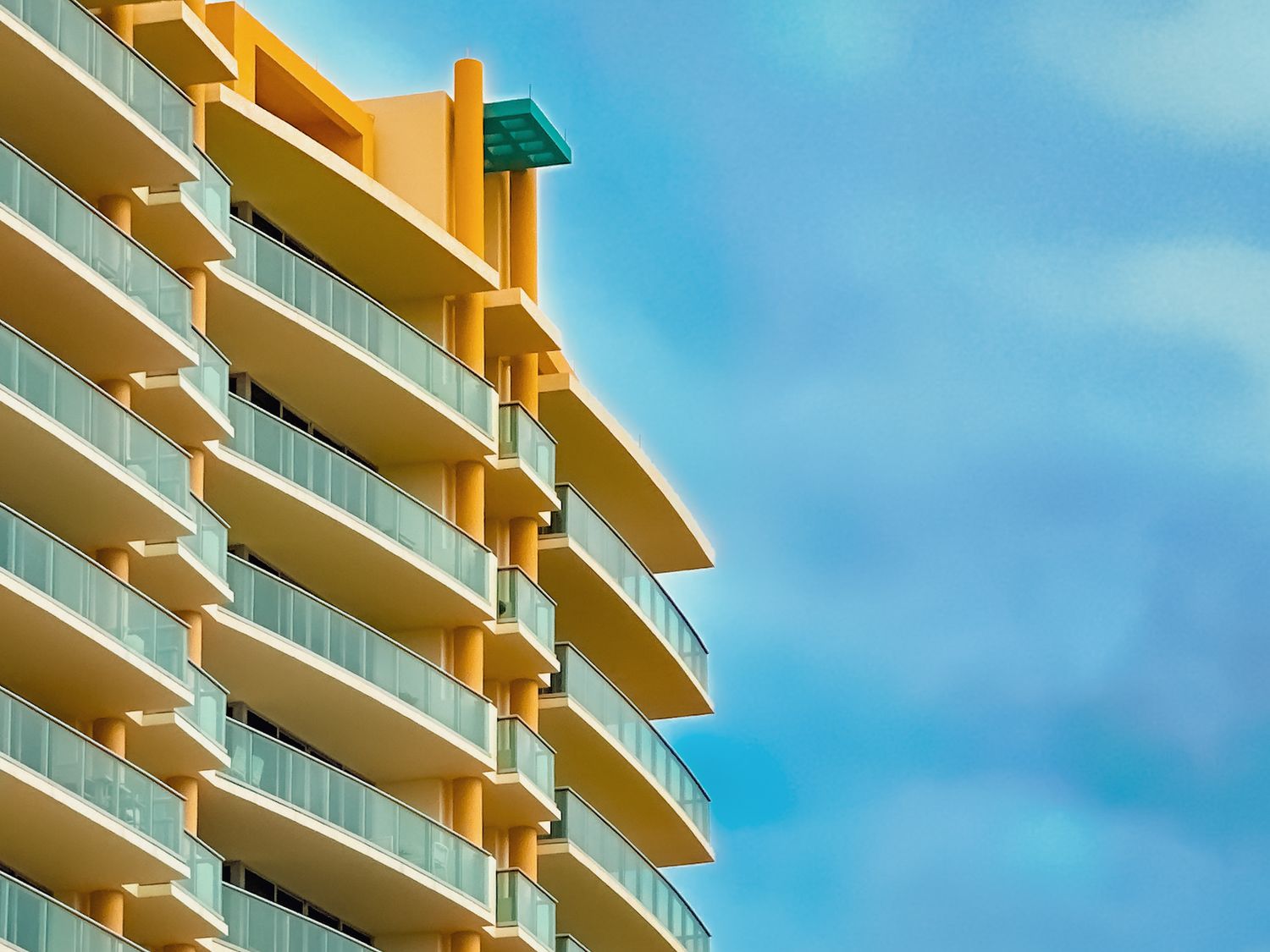 Modern beige apartment building with balconies against bright blue sky.