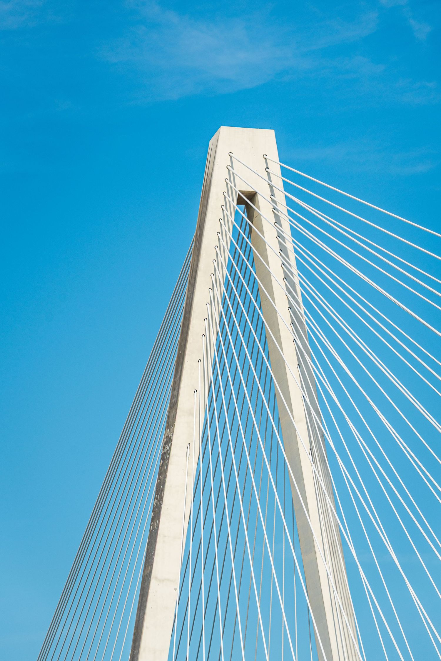 Modern cable-stayed bridge towers against bright blue sky with geometric white support cables.