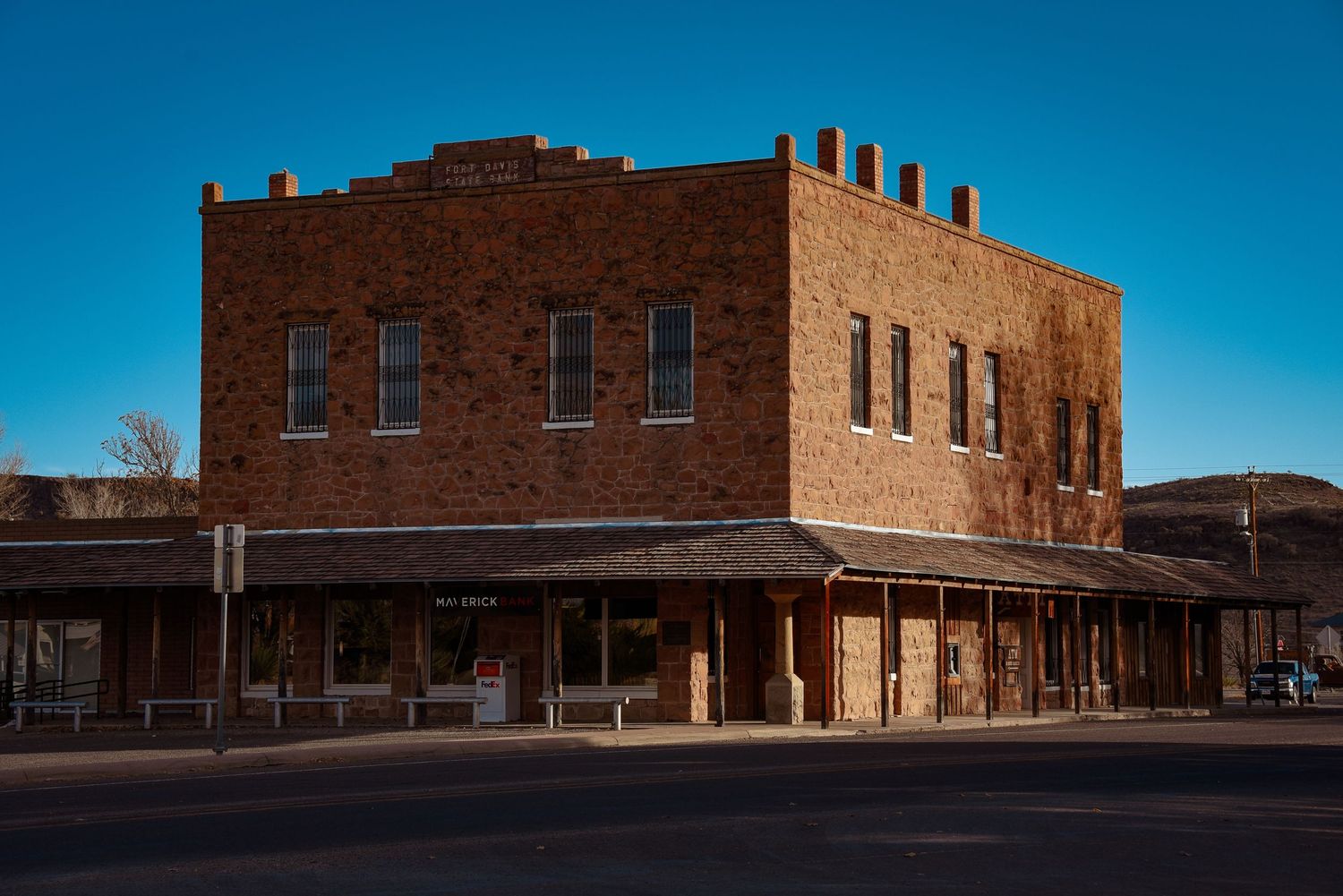 Historic brick commercial buildings line a desert town street under bright blue skies.