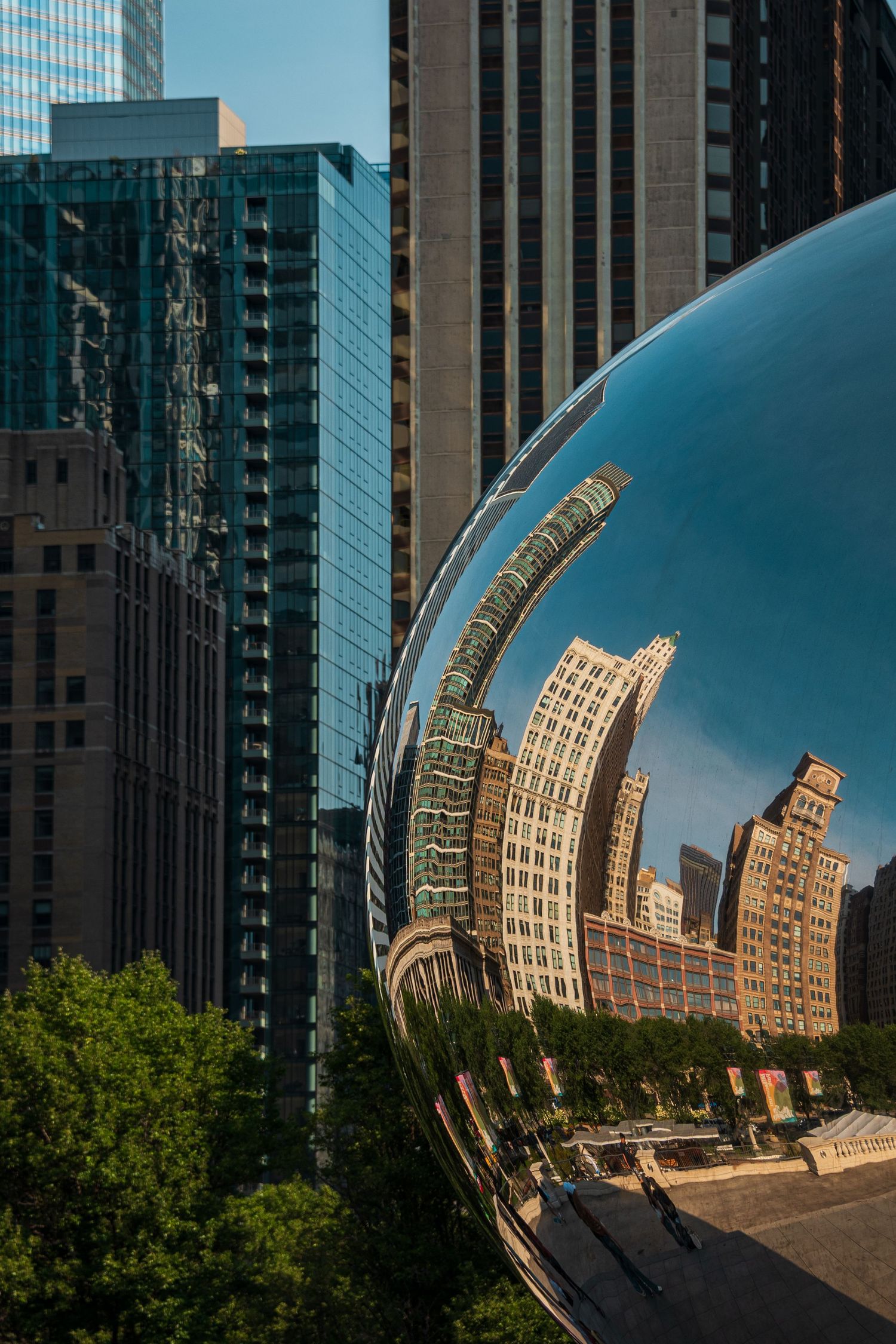 Curved reflective sculpture mirrors distorted city buildings in urban setting.