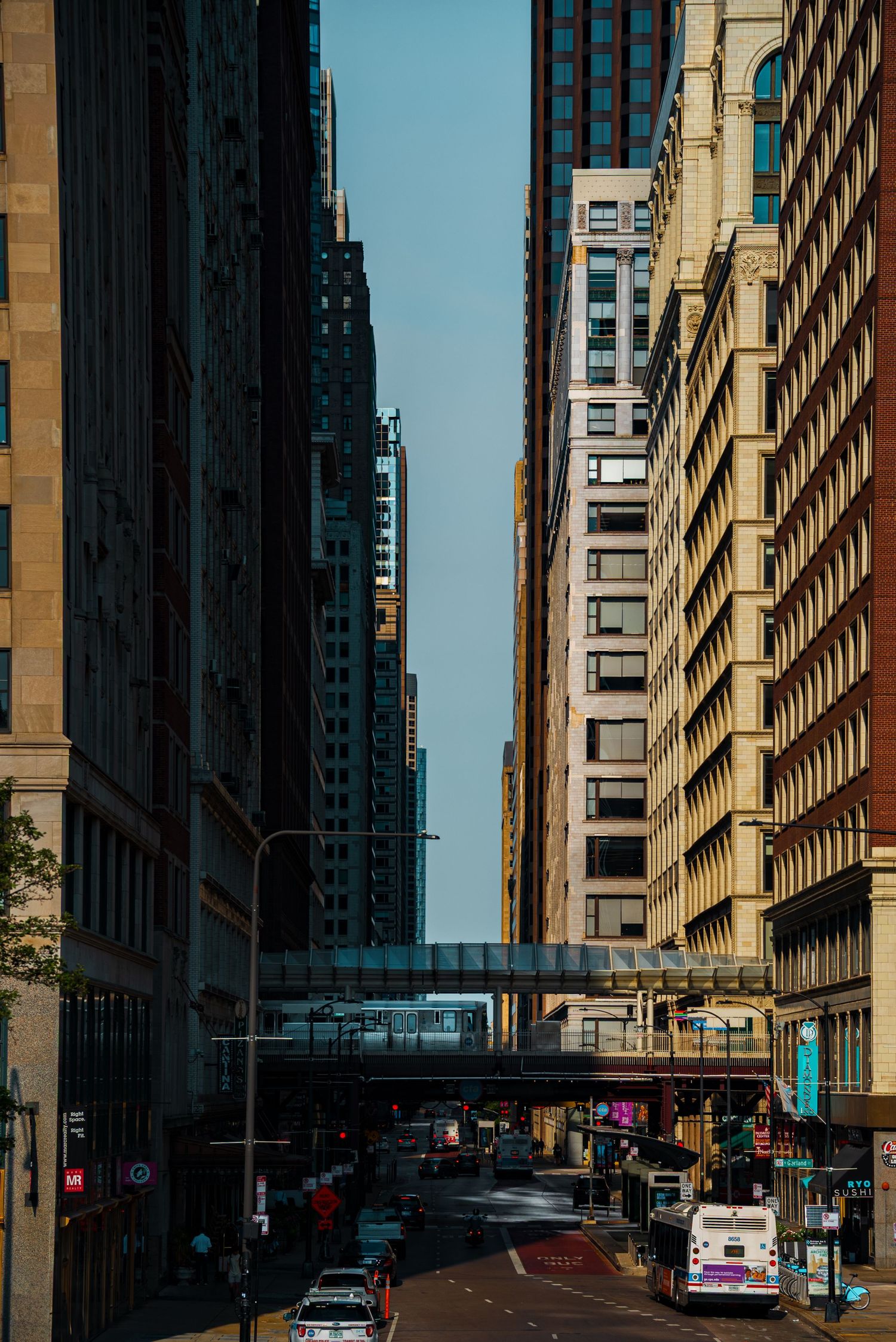 Urban canyon view of tall buildings lining a city street with dramatic shadows and sunlight.